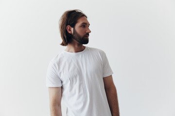 Portrait of a man with a black thick beard and long hair in a white T-shirt on a white isolated background emotion of sadness and longing