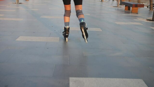 Woman wearing safety protection pads learning to roller skate in summer park.