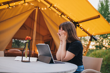 Happy Woman freelancer  using a laptop on a cozy glamping tent in a sunny day. Luxury camping tent for outdoor summer holiday and vacation. Lifestyle concept
