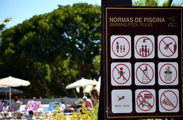 Schild mit Pool-Regeln mit Badegästen im Hintergrund