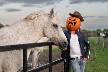 Mann mit geschnitzten Kürbis auf dem Kopf verkleidet als Cowboy neben Pferden an Halloween