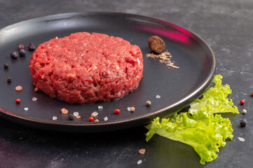 Chopped Steak With Nutmeg And Pappercorns On A Black Plate. The Hamburger Is Ready To Fry. Minced Beef. Fresh Lettuce Leaf As Garnish. Culinary Preparation. Side View. Close Up. Selective Focus.