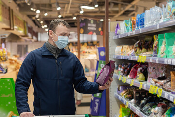 A man in a protective face mask chooses products in the store. Food and drinks. Groceries