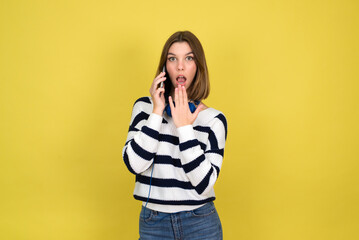 Portrait of cute happy teenage girl wearing talking on mobile phone and smiling  over yellow background. Copy space.