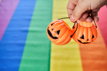 Two Halloween pumpkin head baskets hanging by fingers with lgbt pride flag on background