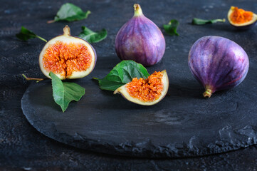 Fresh figs whole and cut into pieces on black slate. Autumn fruits. Front view, selective focus, daylight