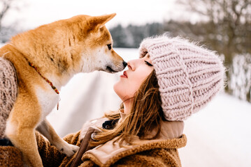 Cute young girl is having fun in winter park with her dog on bright day. Woman relaxing outdoors