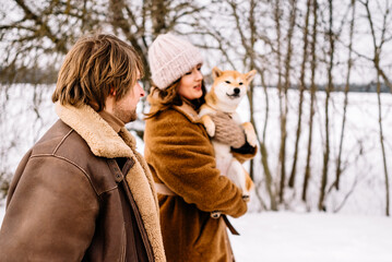 Cute young couple having fun in the winter park with their dog on bright day.Man and woman are relaxing