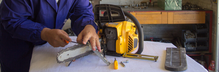 Image of a handyman who sharpens the chain of a chainsaw with a file. Preparation of tools for cutting wood in anticipation of winter. Do-it-yourself work. Horizontal banner 
