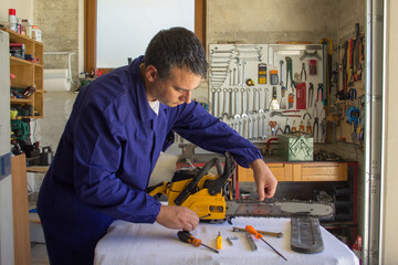 Image of a mechanic in his garage repairing a chainsaw by tensioning the chain. Do-it-yourself work in anticipation of the winter season
