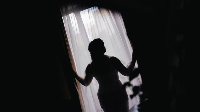 The silhouette of a girl with a large figure standing in a negligee in front of the window. Interesting light on the silhouette