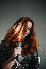 Portrait of redhead female singer woman in sparkly evening dress holding microphone. Singer at microphone. Woman singing and holding mic. Female vocal talent. Music show recital.