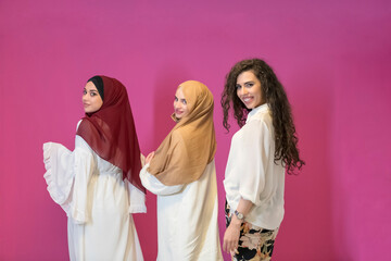 three Muslim women in hijab in a modern clothes pose against a pink background
