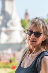 Vertical photo of mature blonde woman with glasses looking at the camera. Behind out of focus...