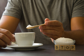 Male hand holding wooden spoon with sugar over cup of coffee or tea. Stop sugar. Campaign against diabetes, obesity, dental caries. Reduce sugar intake. - obrazy, fototapety, plakaty