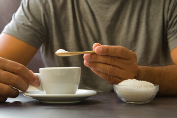 Male hand holding wooden spoon with sugar over cup of coffee or tea. Stop sugar. Campaign against...