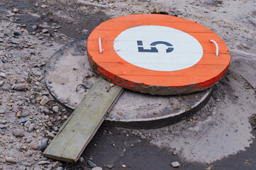 The sewer manhole at the construction site is covered with a round orange sign with the number...