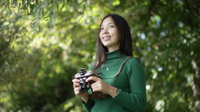 Young slim woman with teeth braces laughing looking away standing with photo camera outdoors. Live camera panning left to right as beautiful Asian talented lady admiring nature in park