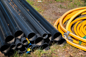 Plastic black pipes lying on the ground next to a roll of yellow cable.