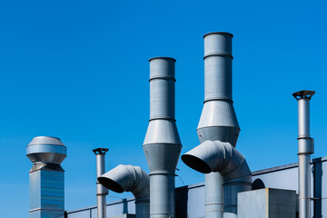 Ventilation pipes of an industrial building against the blue sky.