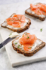 Wholewheat bread sandwiches with cream cheese and smoked salmon on marble board with lime slices and sour cream