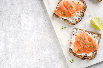 Wholewheat bread sandwiches with cream cheese and smoked salmon on marble board with lime slices and sour cream. top view, space for text