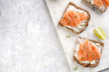 Wholewheat bread sandwiches with cream cheese and smoked salmon on marble board with lime slices...