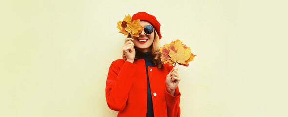 Autumn portrait of happy smiling young woman with yellow maple leaves wearing red french beret on gray background