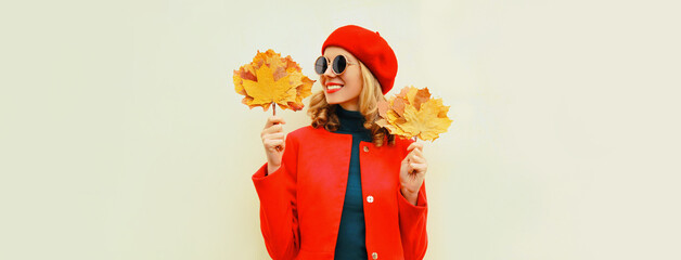 Autumn portrait of happy smiling young woman with yellow maple leaves wearing red french beret on gray background