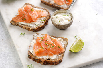 Wholewheat bread sandwiches with cream cheese and smoked salmon on marble board with lime slices and sour cream