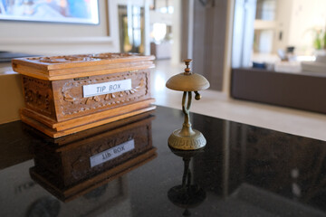 Brown wooden tip box with antique silver call bell on reception service desk counter, copy space.