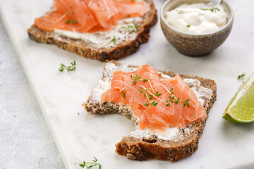 bitten off Wholewheat bread sandwiches with cream cheese and smoked salmon on marble board with...