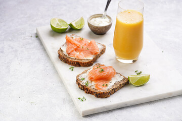 Wholewheat bread sandwiches with cream cheese and smoked salmon on marble board with orange juice, lime slices and sour cream