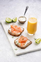 Wholewheat bread sandwiches with cream cheese and smoked salmon on marble board with orange juice, lime slices and sour cream