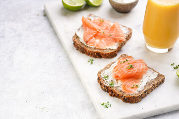 Wholewheat bread sandwiches with cream cheese and smoked salmon on marble board with orange juice, lime slices and sour cream