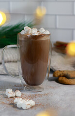 hot chocolate in a glass mug with mini marshmallows on grey table, blurred xmas background 