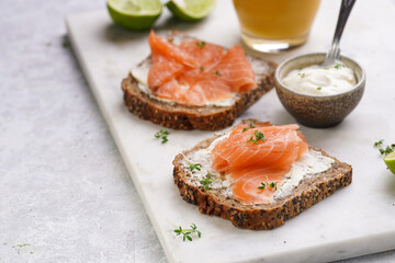 Wholewheat bread sandwiches with cream cheese and smoked salmon on marble board with orange juice, lime slices and sour cream