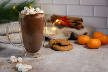 hot chocolate in a glass mug with mini marshmallows on grey table, blurred xmas background 