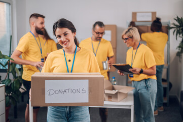 Portrait of a volunteer holding cardboard box with his colleagues in the background