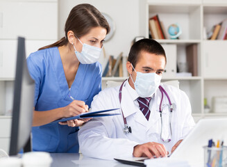 Doctor and nurse in protective medical mask check patient data in hospital computer database