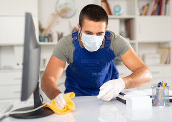 Professional worker of office cleaning service wearing protective face mask and rubber gloves wiping desk with disinfectant - Powered by Adobe