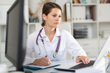 Cheetful woman doctor sitting at workplace with computer in her office