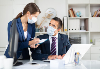 Manager in protective medical mask gives task to assistant at office