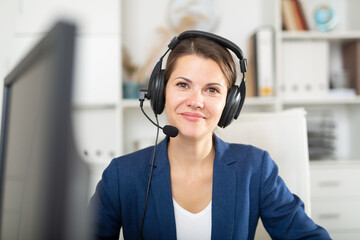 Portrait of smiling young woman helpline operator with headphones during work in call center