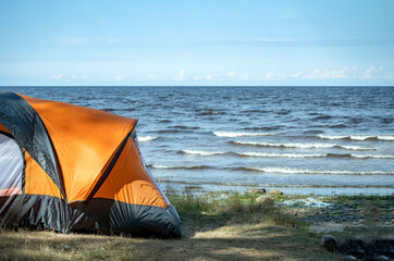 The edge of a tourist tent on the shore against the background of the exciting sea. Camping, camping, survival in the wild, outdoor living.