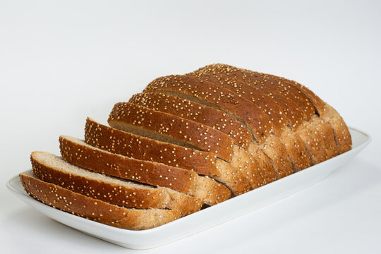 Pão integral fatiado coberto com sementes, sobre uma travessa branca em um fundo branco isolado