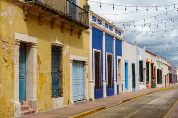 Colorful old buildings line a narrow street in Campeche. There are string lights overhead.