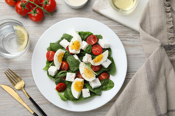 Delicious salad with boiled eggs, feta cheese and tomatoes served on wooden table, flat lay