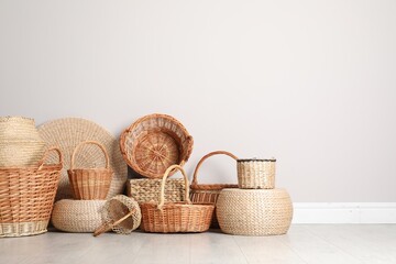 Fototapeta premium Many different wicker baskets made of natural material on floor near light wall. Space for text