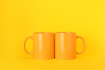 Two blank ceramic mugs on yellow background